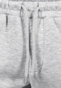 Lichtgrijze sweatpants van zacht, textuurachtig materiaal, met een elastische tailleband en een trekkoord met een gevlochten ontwerp. Twee zijzakken.