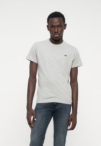 Grå bomull T-skjorte med korte ermer, med en liten svart "Lee" logo på brystet. Modellen har på seg mørkeblå jeans.