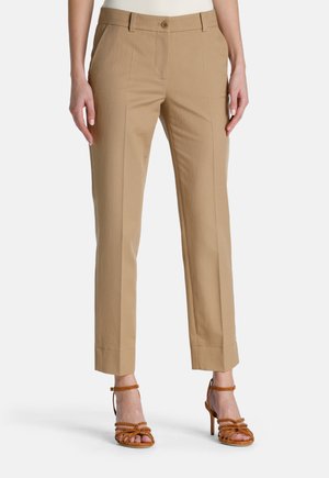 Pantalon beige ajusté à coupe droite, avec un ourlet à revers, deux poches avant et une fermeture à un bouton, associé à des talons bruns à lanières.
