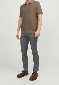 Camisa polo marrón de manga corta con diseño de punto texturizado, combinada con pantalones grises ajustados y zapatos marrones oscuros con cordones.