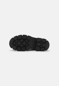 Semelle de chaussure en caoutchouc noir avec des motifs de profondeur, des sections moulées et un bord plat pour une traction et une durabilité accrues.