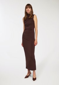 Brązowa sukienka bez rękawów o dopasowanym kroju, z zasłoniętym materiałem i długości do kolan. Połączona z brązowymi szpilkami z ostrym noskiem.