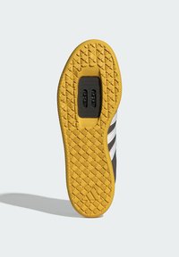 Semelle de chaussure en caoutchouc jaune texturé, avec un insert en plastique noir et un motif de motifs hexagonaux. Rayures blanches le long du bord.