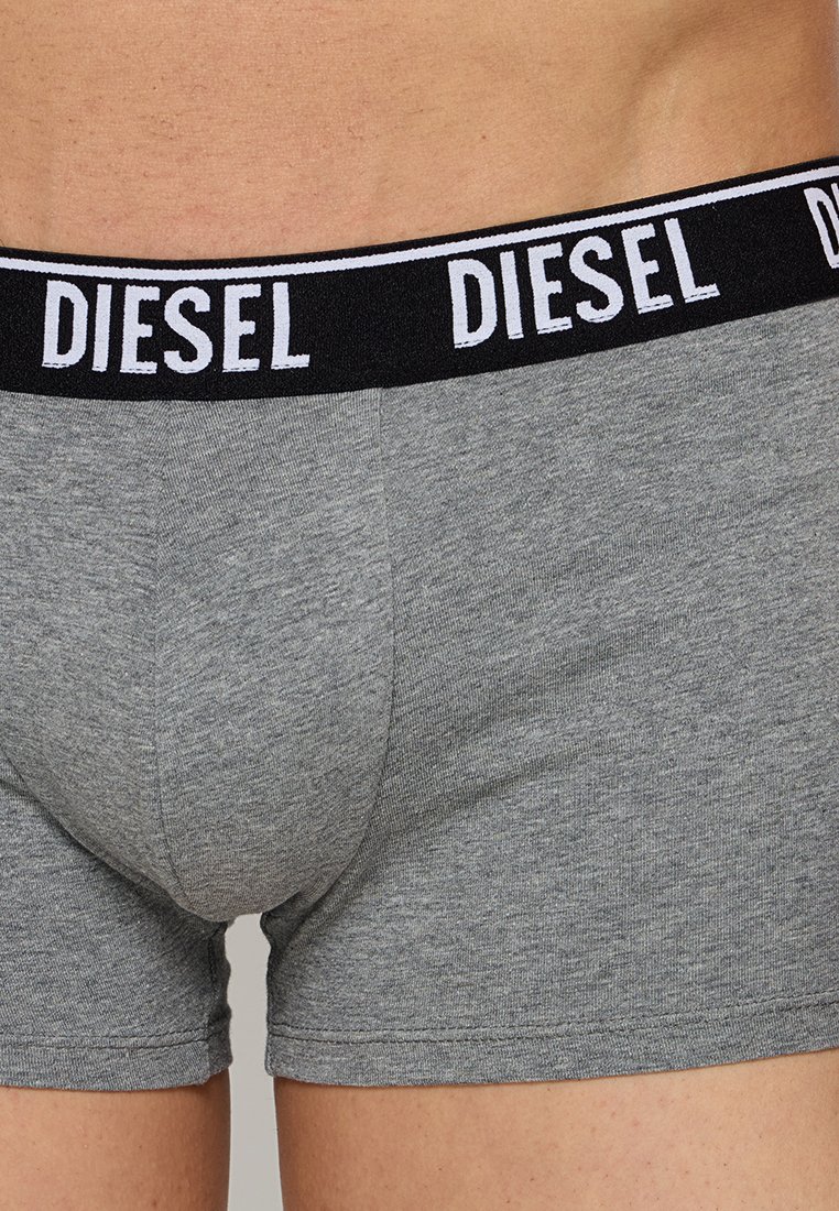 Gros plan sur une personne portant des boxers gris Diesel avec une ceinture noire arborant le logo Diesel en lettres blanches.