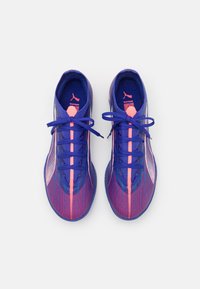 Des chaussures de sport violettes et roses avec une tige en maille texturée, des détails réfléchissants et des lacets ronds. Elles présentent une semelle intérieure rembourrée et une semelle en caoutchouc.