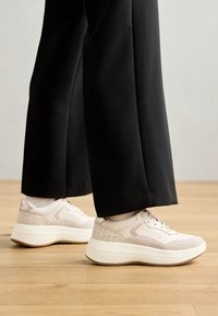 Sneakers med en kombinasjon av lys rosa og beige materialer, med en teksturert bakdel, rund tå og tykk hvit såle.