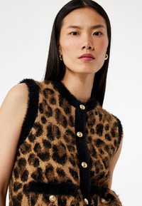 Fuskpälsväst med leopardmönster i brunt och svart, utrustad med guldfärgade knappar och svart kant runt halsringningen och armhålorna.