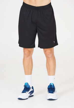 Sorte atletiske shorts med elastisk talje, løs pasform og sidelommer. Sammen med hvide sokker og blå-hvide sportssko.