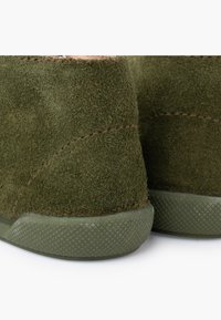 Green suede footwear with a textured, matte finish. Features a rubber sole with a diamond pattern and stitched detailing along the edges.