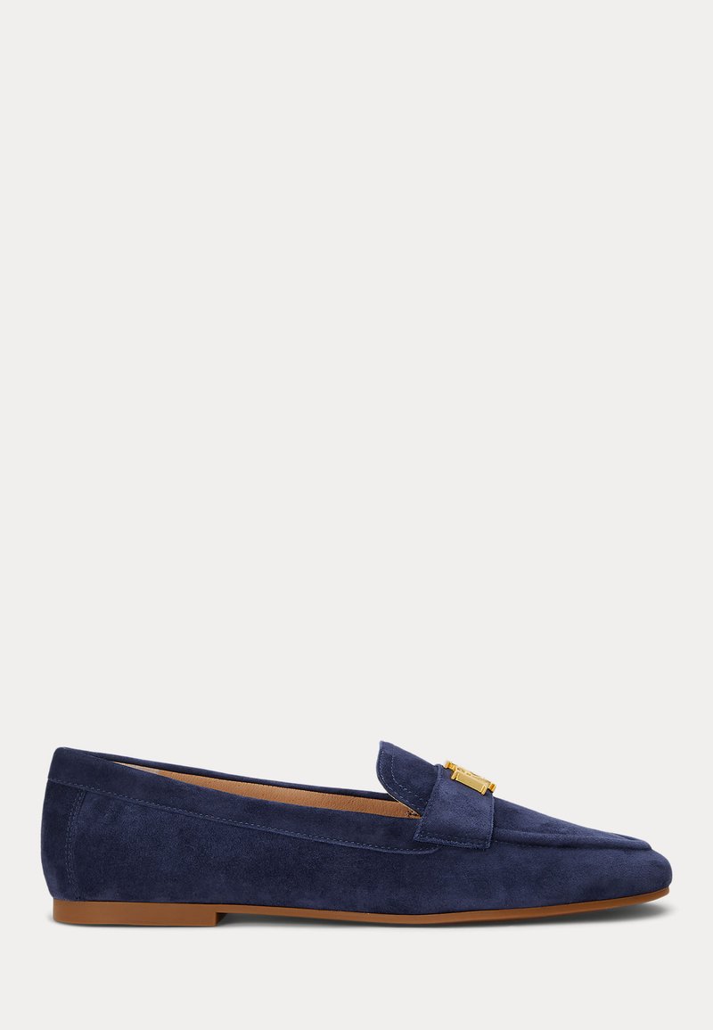 Mocassins em camurça azul-marinho com bico arredondado, sola plana e detalhe em hardware dourado na parte da frente. Textura suave.