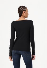 Top lungo nero a maniche lunghe con scollo ampio, aderente in vita, realizzato in materiale morbido. Indossato con jeans blu scuro.