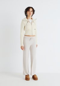 Cropped cream knit jacket with zippered pockets, paired with light gray and white striped wide-leg pants and brown platform shoes.