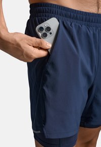 Granatowe sportowe szorty o gładkiej fakturze mają boczną kieszeń mieszczącą smartfon, elastyczny pas i kontrastową podszewkę wewnętrzną.