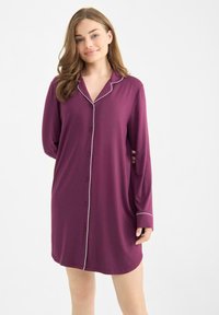 Vestido de pijama púrpura hecho de tela suave, con cierre de botones en el frente, ribete blanco en el cuello y los puños, y mangas largas.