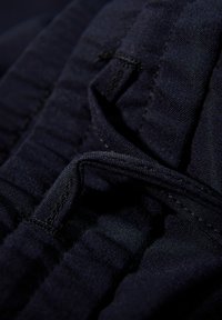 Gros plan sur un tissu marine avec une texture froncée, mettant en valeur les détails de couture et un élément de boucle proéminent pour le réglage ou le maintien.