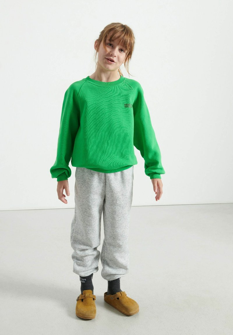 Felpa verde con colletto a costine, pantaloni della tuta grigi e scarpe marroni. Tessuti morbidi, vestibilità rilassata e stile casual.