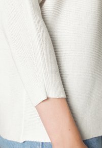 Strickpullover in Off-White mit einem strukturierten Muster, ausgestattet mit Dreiviertelärmeln und einem lässigen Schnitt. Die Kanten sind leicht verarbeitet.