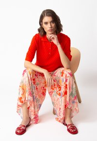 Red knitted polo shirt with short sleeves, paired with floral, semi-sheer palazzo pants in pink and multicolor. Strappy red flat sandals.