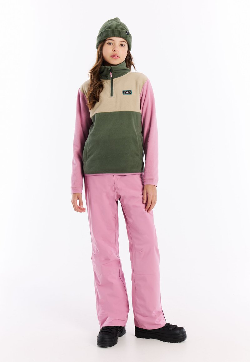 Fleecejack met groene, beige en roze kleurvlakken, half-rits kraag, gecombineerd met roze waterdichte broek en zwarte laarzen.