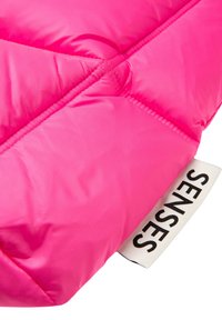 Helles pinkes gesteppte Gewebe mit sichtbarem diagonalen Stich und einem weißen Etikett mit der Aufschrift "SENSES" in schwarzen Buchstaben.