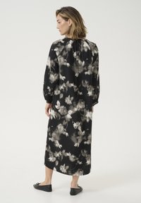 Largo vestido negro con un estampado floral en tonos de gris y blanco. Tejido suave con escote fruncido y aberturas laterales. Combinado con bailerinas negras.