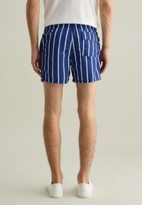 Costumi da bagno blu navy con strisce verticali bianche, vita elasticizzata, tasche laterali e tasca sul retro. Tessuto liscio e a rapida asciugatura.