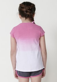 Camiseta de manga corta en degradado rosa y blanco, hecha de algodón suave, con un escote redondeado y aberturas laterales para facilitar el movimiento.