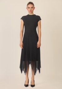 Vestido negro con un cuerpo ajustado y una falda plisada y fluida. Presenta un escote alto y un dobladillo asimétrico, hecho de una tela ligera.