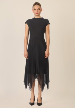 Schwarzes Kleid mit enganliegendem Oberteil und plissiertem, fließendem Rock. Hat einen hohen Ausschnitt und einen asymmetrischen Saum, aus leichtem Stoff gefertigt.