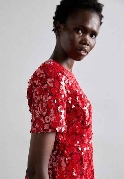 Robe en sequins rouges avec des embellissements floraux, manches courtes, col rond et détails intriqués. Texture lisse et finition brillante.