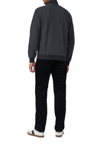 Dunkelgrauer, strukturierter Pullover mit hohem Kragen, kombiniert mit schwarzen Cordhosen und weißen Sneakers mit braunen Akzenten.