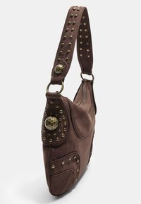 Braune Wildleder-Handtasche mit einem Reißverschluss, verziert mit Nietenakzenten und einem runden Metallknopf. Sie hat einen breiten Schultergurt.