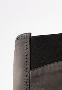 Botte en cuir gris à surface texturée, dotée d'un panneau latéral élastique noir et de détails perforés le long du bord supérieur.