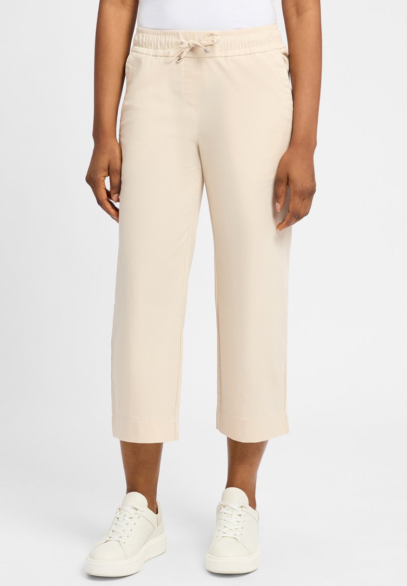 Beige cropped broeken met een elastische tailleband, trekkoorddetail en zijzakken, gecombineerd met witte sneakers. Gladde stoftextuur.