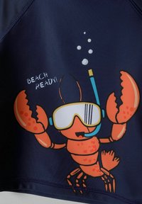 Maillot de bain marine avec un vibrant homard en dessin animé portant un équipement de snorkeling et le texte "PRÊT POUR LA PLAGE !" en police ludique blanche.