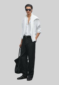 White button-up shirt, lightweight sweater draped over shoulders, black wide-leg trousers, black sandals, carrying a large black tote bag.
