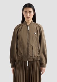 Giacca bomber marrone con zip frontale, vita elasticizzata, tasche laterali, texture liscia e un piccolo logo sul petto.