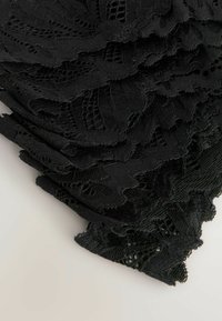 Țesătură din dantelă neagră cu margini ondulate, având modele florale intricate și o suprafață texturată, întinsă pe un fundal neutru.