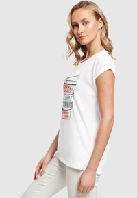 Weißes T-Shirt mit kurzen Ärmeln, das verspielten grafischen Text in Pink und Grün zeigt. Aus weichem Baumwollstoff, lockere Passform mit umgeschlagenen Ärmelsäumen.
