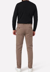 Beige chinos yang pas badan, dilengkapi dengan kantong belakang dan campuran katun yang halus. Dipasangkan dengan atasan hitam lengan panjang dan sepatu sneaker putih.