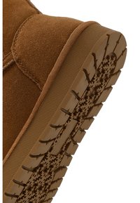 Braune Wildlederstiefelette mit einer strukturierten Gummisohle, die ein Profilmuster für Halt und Langlebigkeit aufweist. Runde Zehenpartie und einfache Nähte.