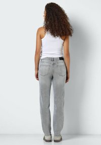 Grey denim jeans with a straight-leg design, five pockets, and a black waistband accent, paired with a white tank top and beige shoes.