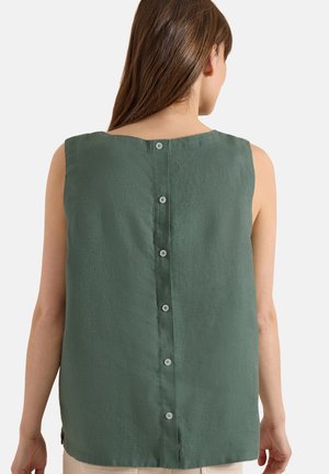 Femme portant un haut vert sans manches avec des boutons dans le dos, montrée de dos sur un fond uni.