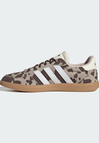 Matalat tennarit, joissa on ruskea ja beige leopardikuvio, valkoiset Adidas-raita, beigen värinen kantapään lenkki ja kumipohja.