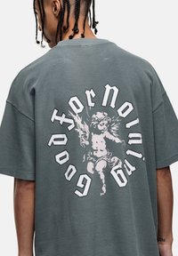 Szary t-shirt o oversize'owym kroju ze strukturą w wafle, z białą grafiką cheruba i wyboldowanym napisem na plecach. Krótkie rękawy i okrągły dekolt.