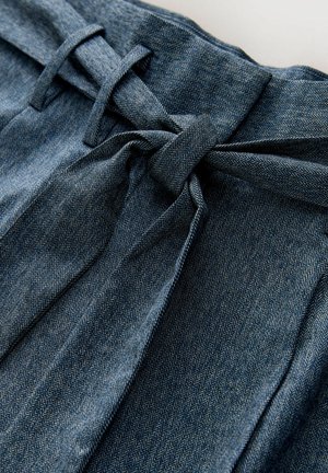 Close-up of blue herringbone fabric pants with a tied self-fabric belt at the waist and belt loops visible.