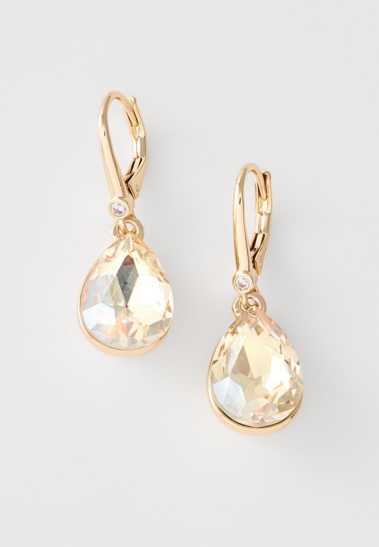 Goldfarbene Ohrringe mit großen, facettierten, tropfenförmigen Kristallen in klarem Finish, akzentuiert durch kleine runde Edelsteine in der Nähe des Hakens.