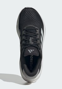 Chaussure de sport noire avec une tige en maille respirante, design à trois bandes blanches, col rembourré et semelle texturée.