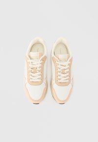 Παπούτσια αθλητικά με λευκό και ανοιχτό ροζ άνω μέρος, διαθέτοντας υφή, στρογγυρά κορδόνια και καουτσούκ σόλα. Ορατά χρυσά μάτια και λογότυπο.