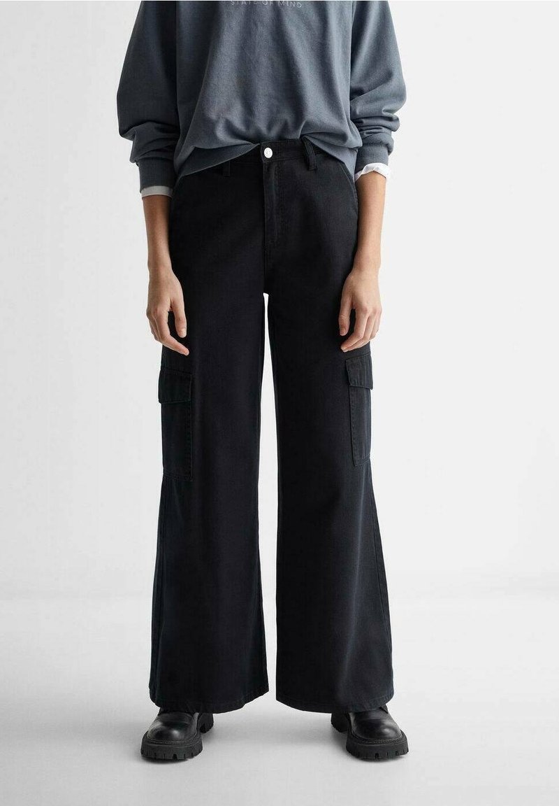 Personne portant un pantalon cargo noir à jambes larges, des chaussures noires épaisses, et un sweat-shirt oversize bleu-gris aux manches retroussées.